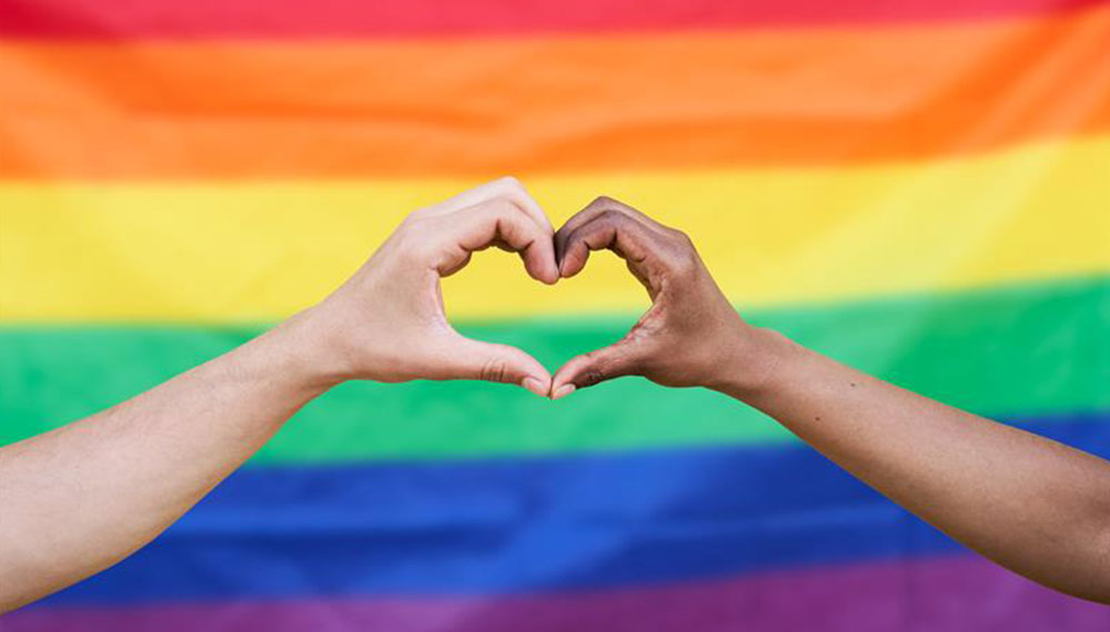 two hands making a heart in front of pride flag